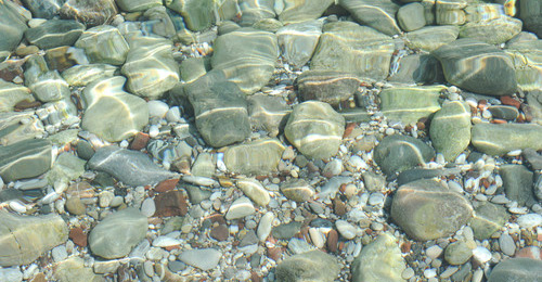 Den Dingen auf den Grund gehen Kieselsteine am Grund eines Wassers mit Lichtreflexionen